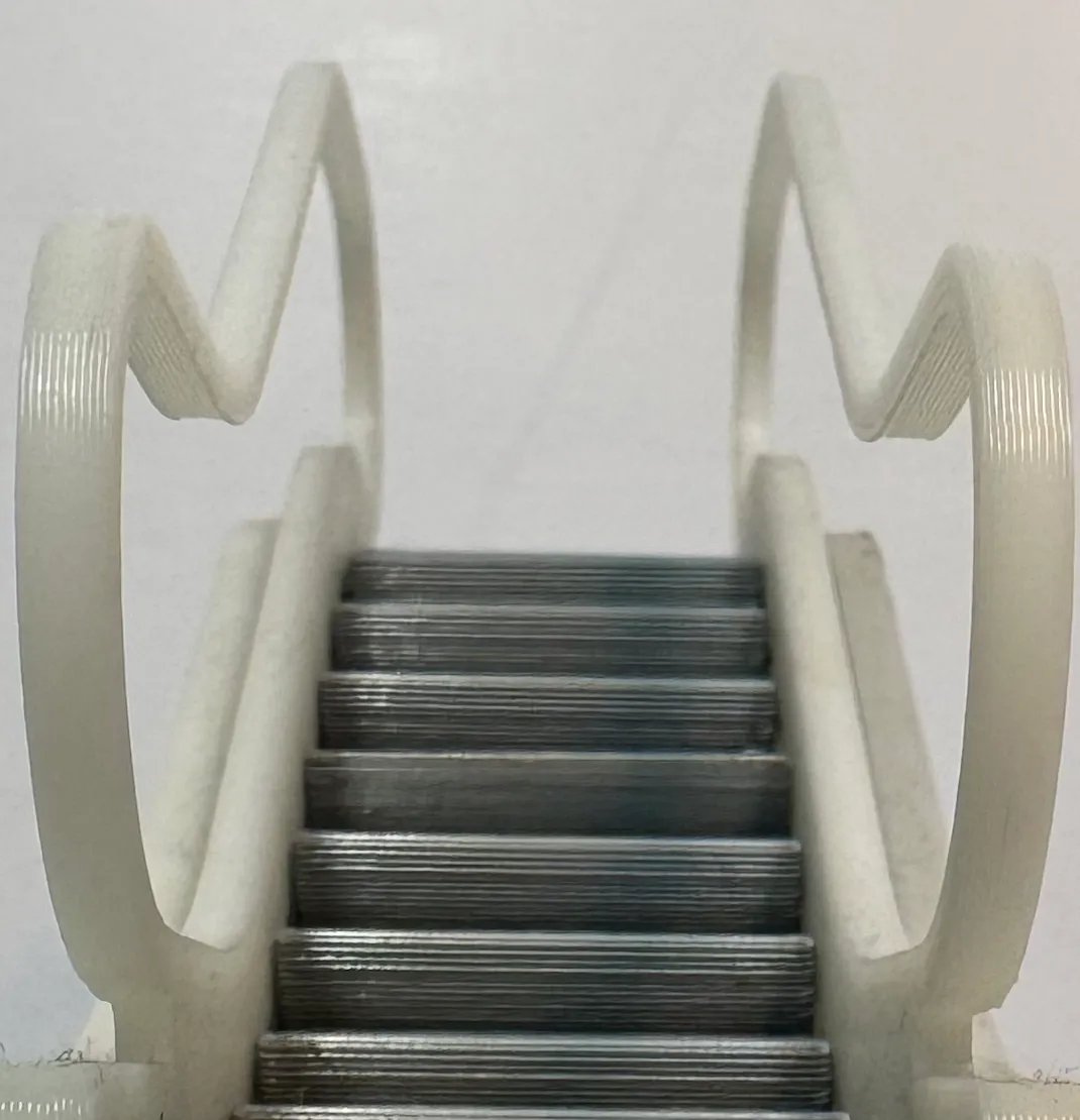 Close-up looking up the escalator: grey printed steps with fine layer lines, between the white looped handrails