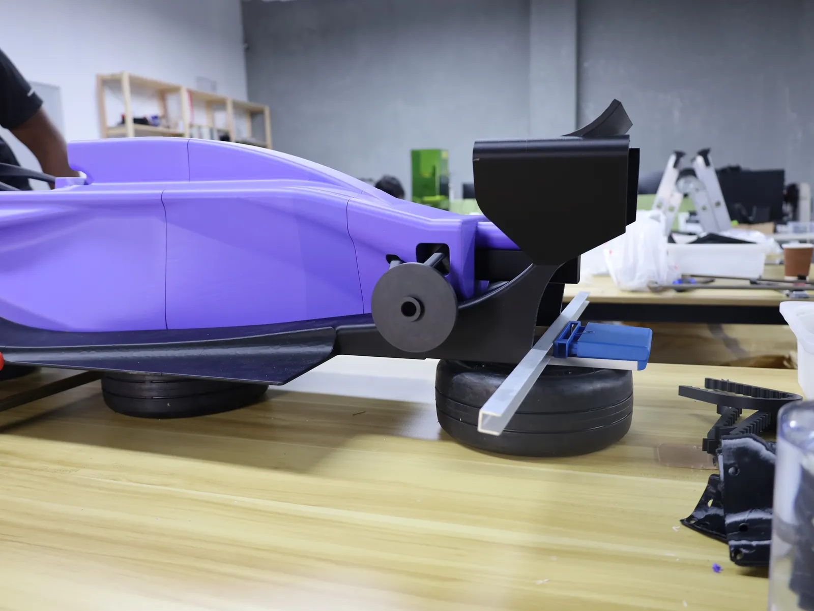 Side view of the rear of the car on the bench: the purple body, a black rear axle disc and the rear wing mount, resting on its tyres