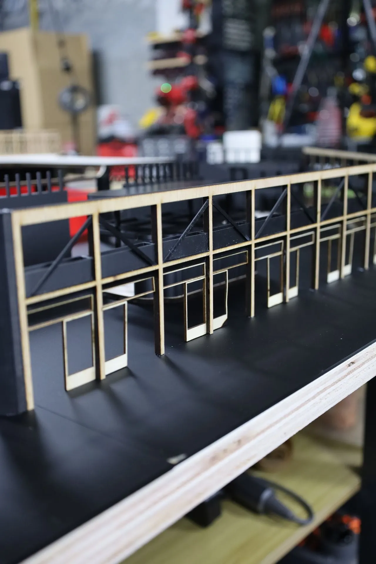 Low view along the rear facade: a long run of plywood door and window frames on the black base