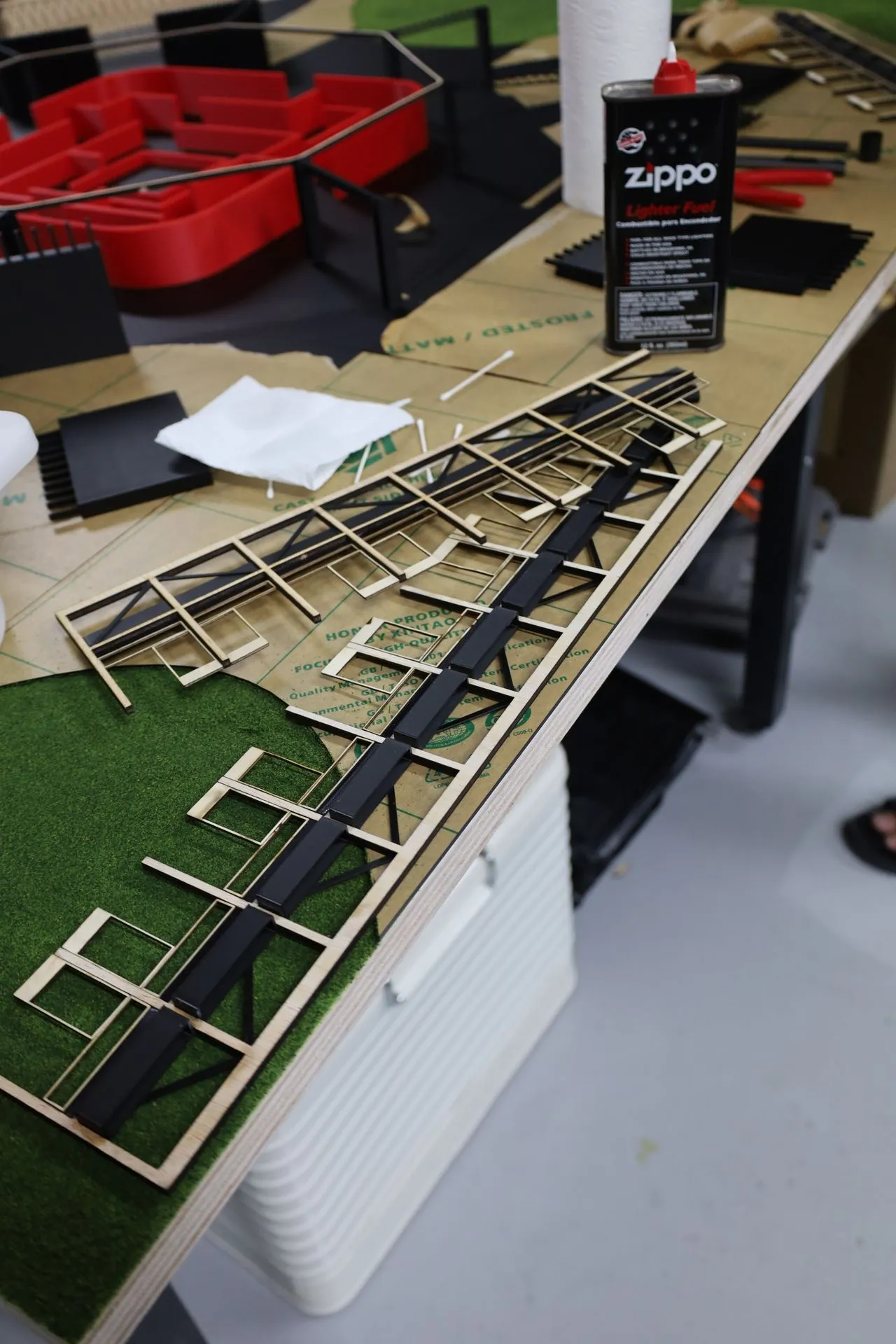 Laser-cut plywood window and door frames laid out on the workbench with black strips glued along them, beside the part-built model