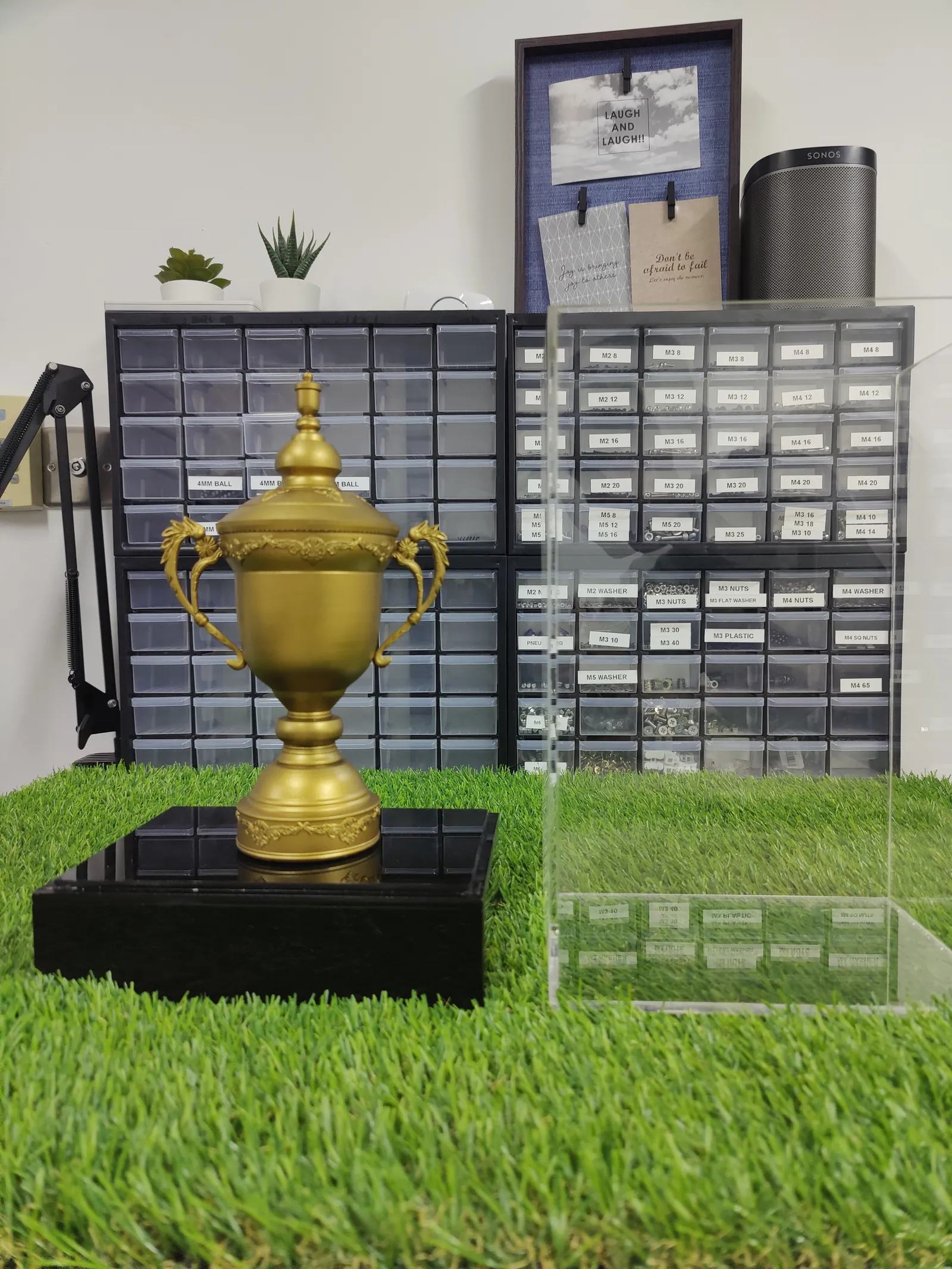 The matte gold replica on its glossy black base, with the clear acrylic case standing beside it