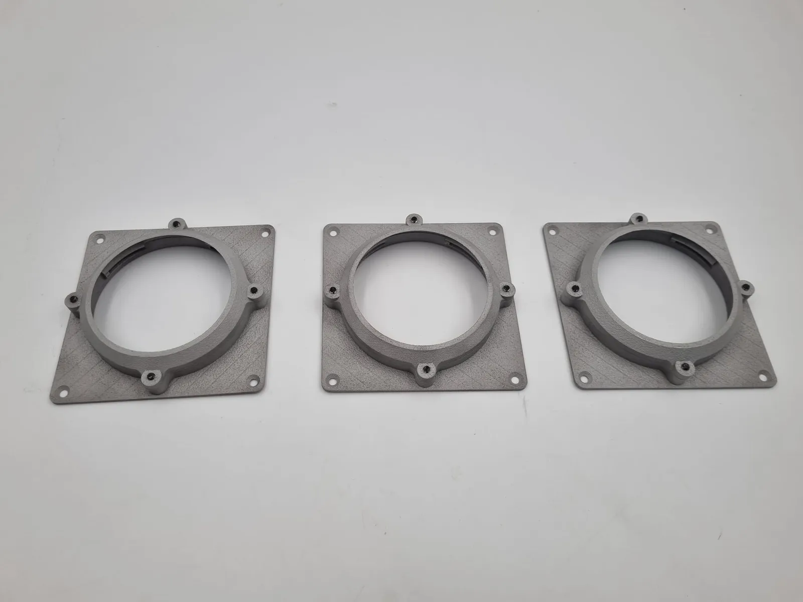 Three grey aluminium panel mounts in a row, each a square plate with corner holes and a round collar with four screw points