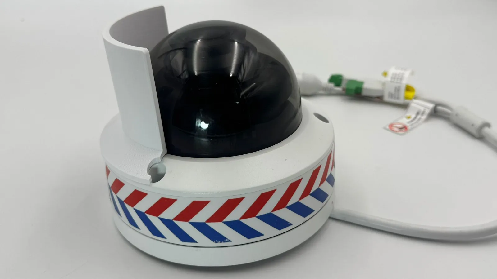 The white shield fitted on the camera's base from the side, its notch framing a screw hole, with the camera's cable behind