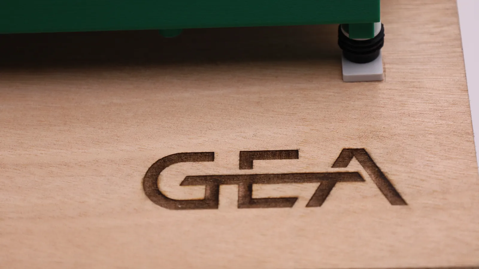 Close up of the GEA logo laser-engraved into the plywood base, next to one of the model's printed feet