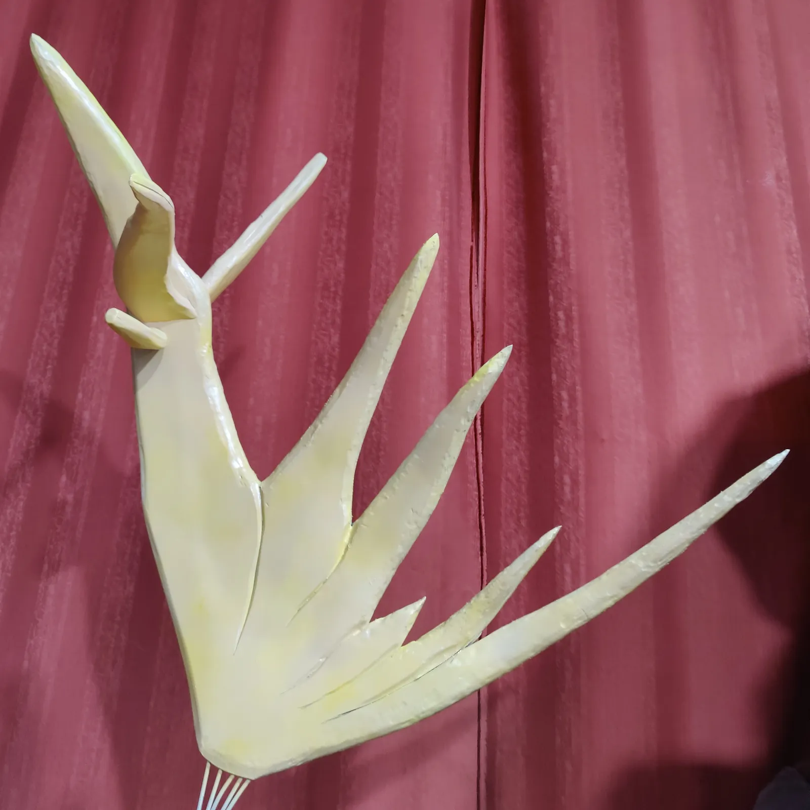 A printed tine with five pointed spikes, unpainted, held up against a red curtain