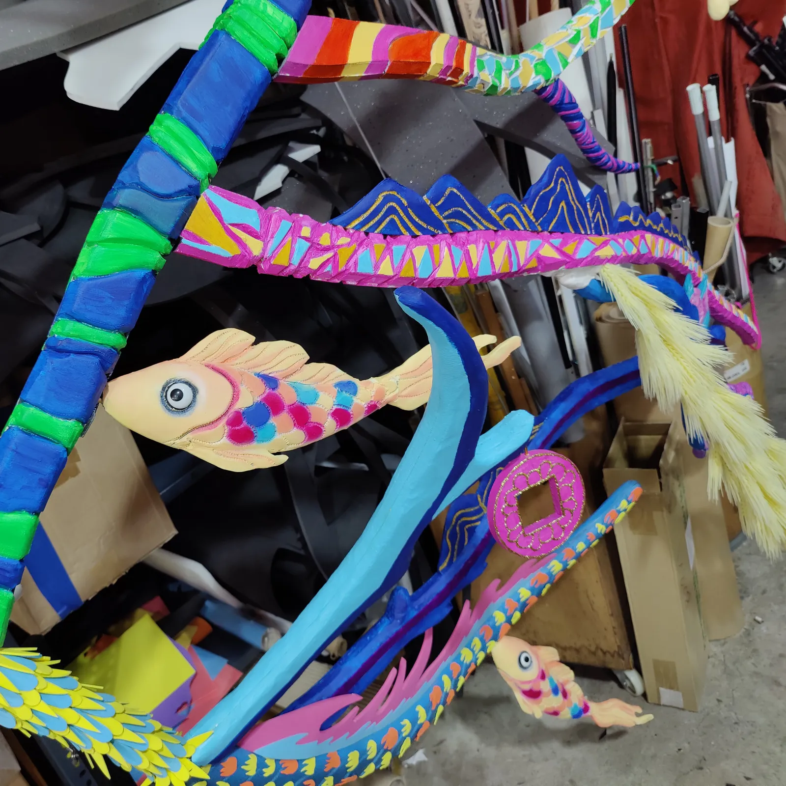 A painted fish in cream, pink and blue among branches striped in bright colours
