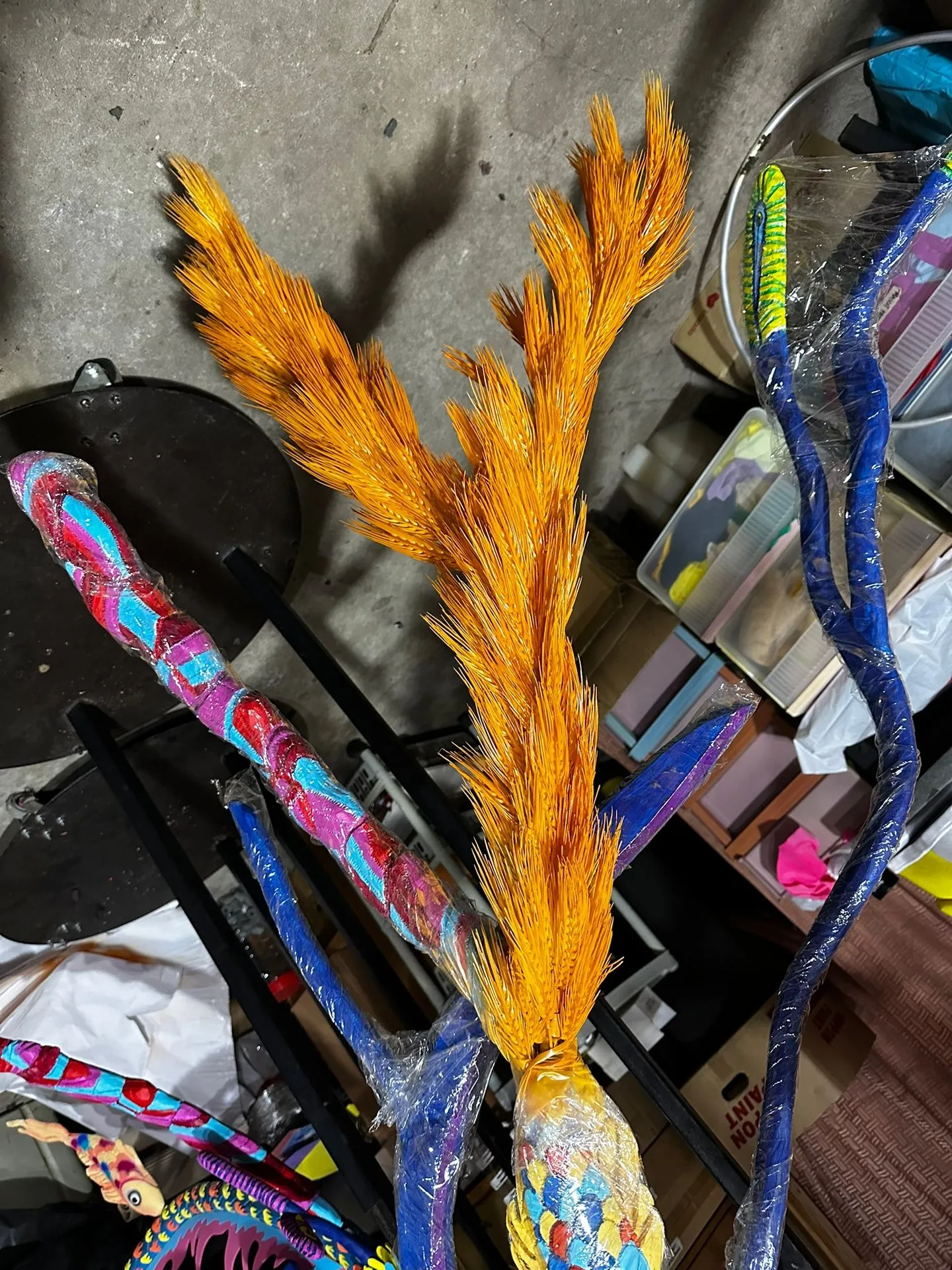 A feathered tine painted in orange and gold above branches patterned in blue, pink and red