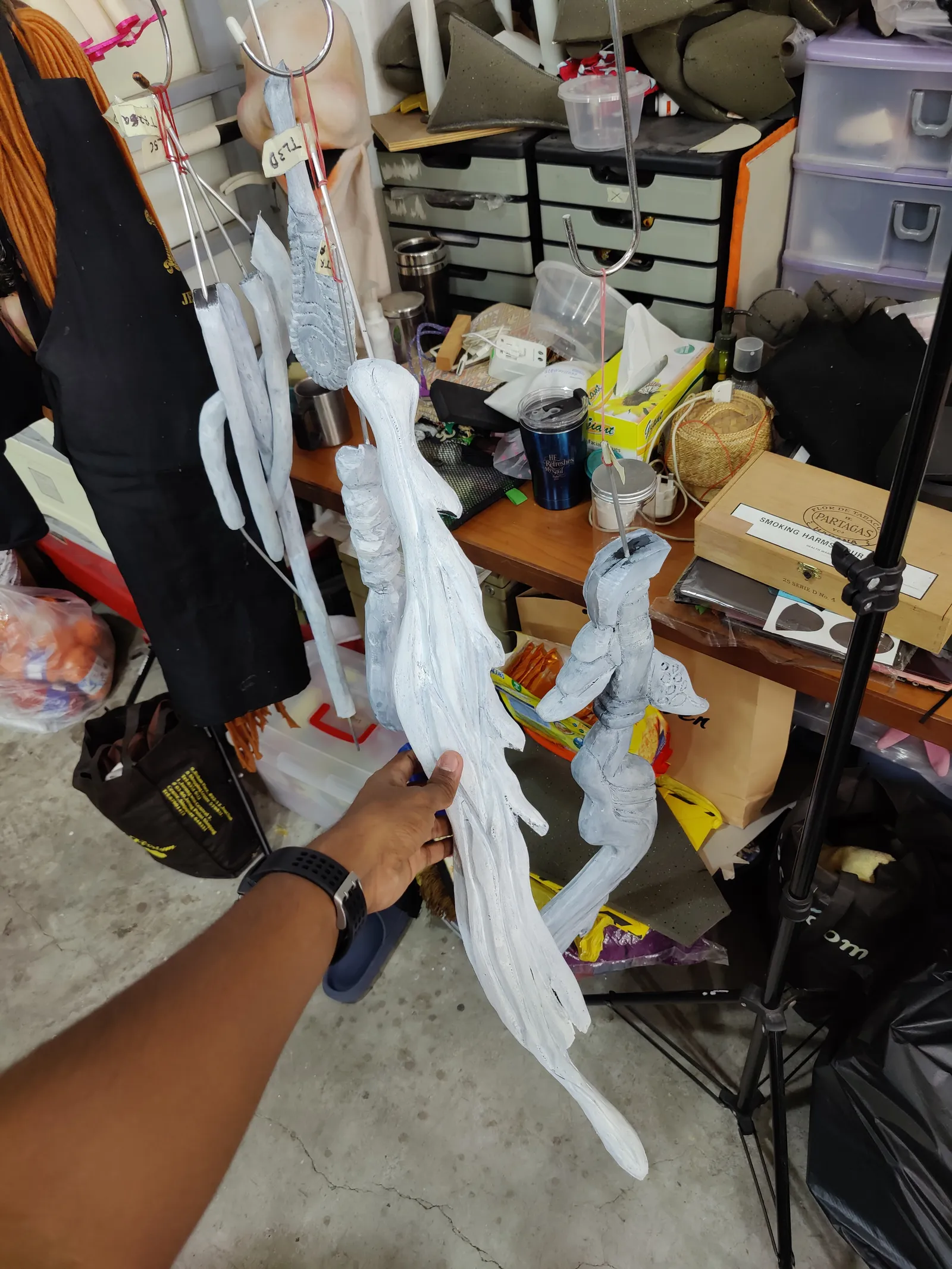 A hand holding up a long white 3D printed branch in the studio, before primer