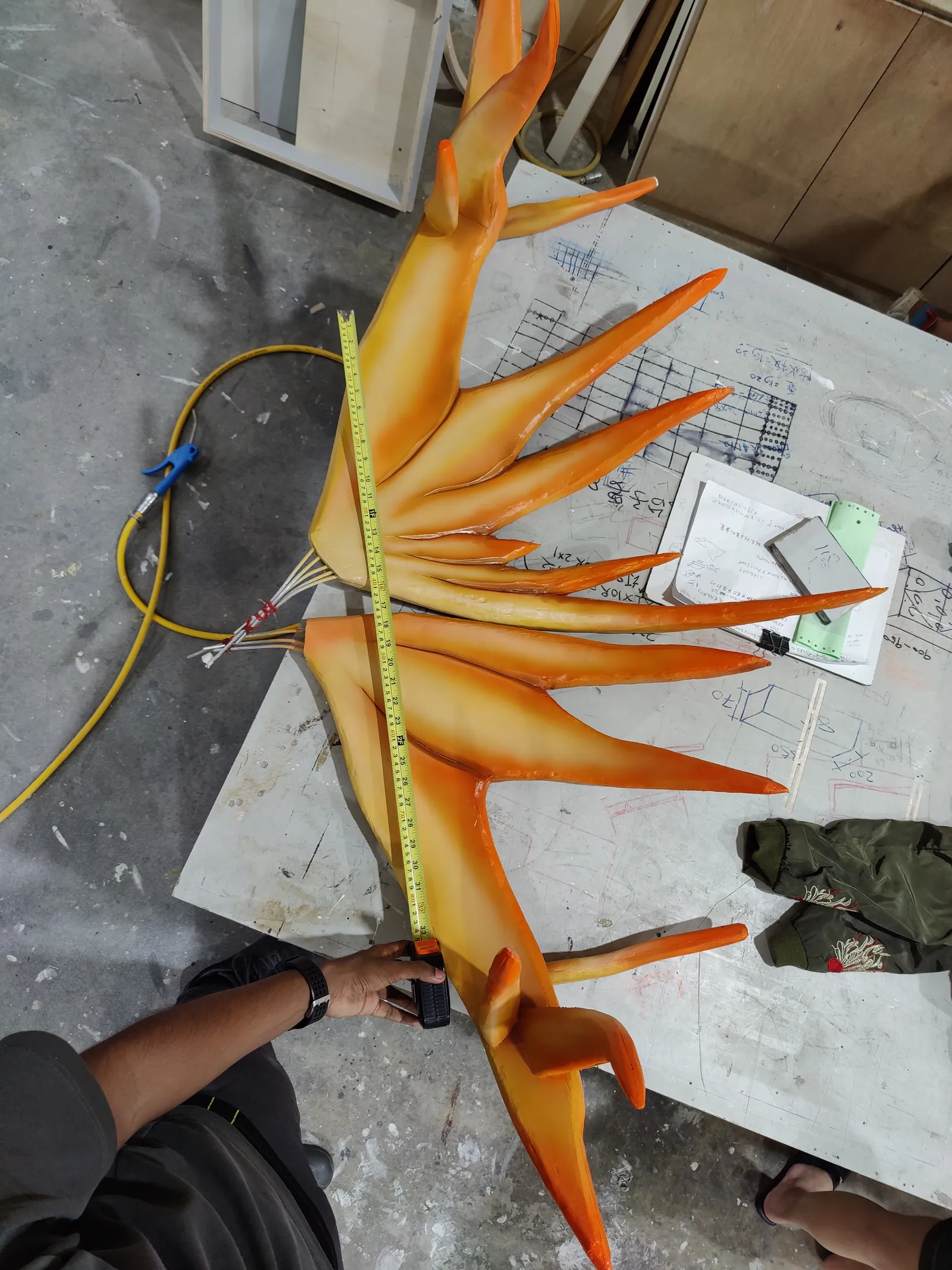 A hand holding a feathered tine painted in orange and yellow over a work table