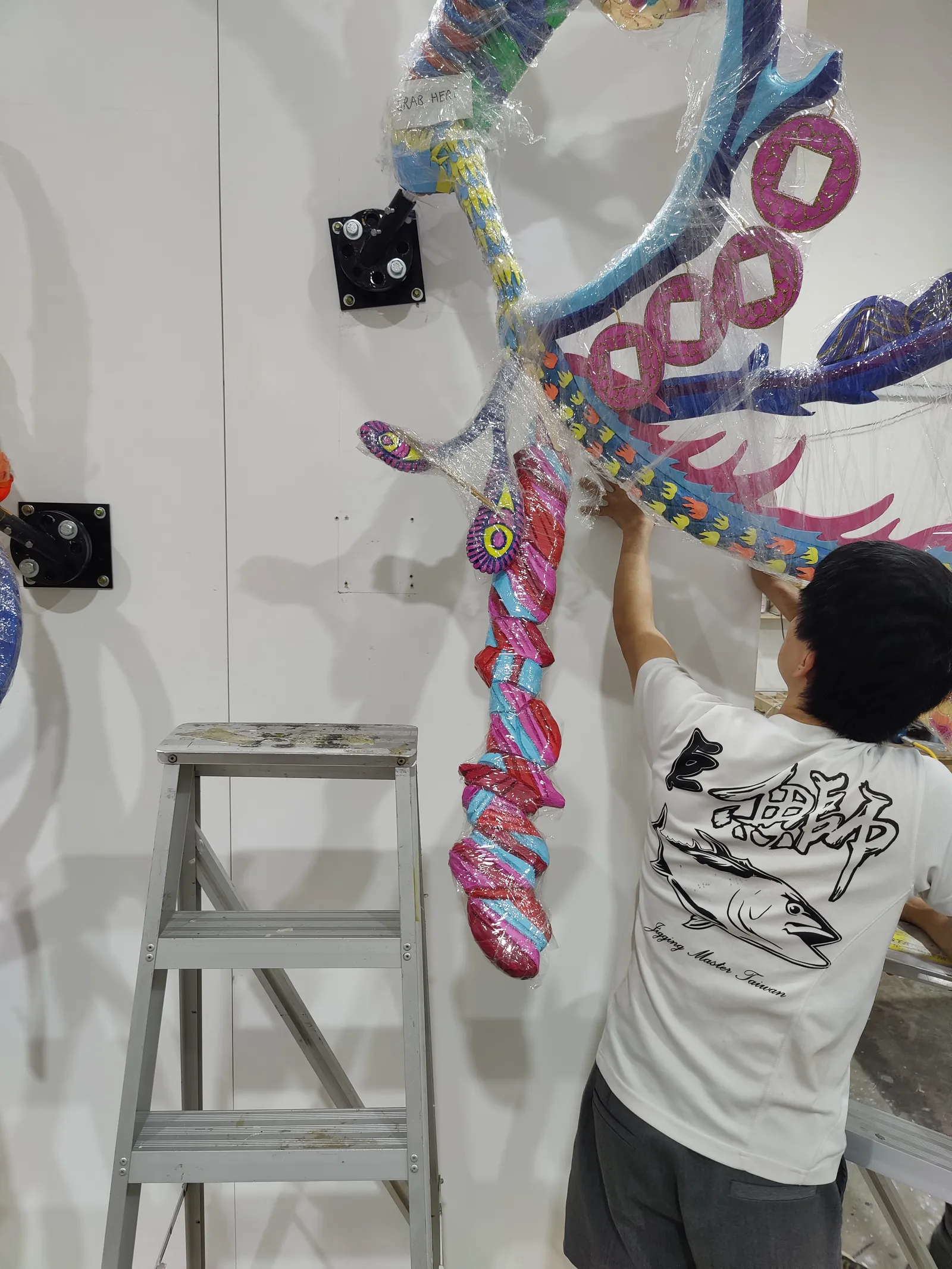 A team member on a stepladder fitting the upper branches beside a wall bracket