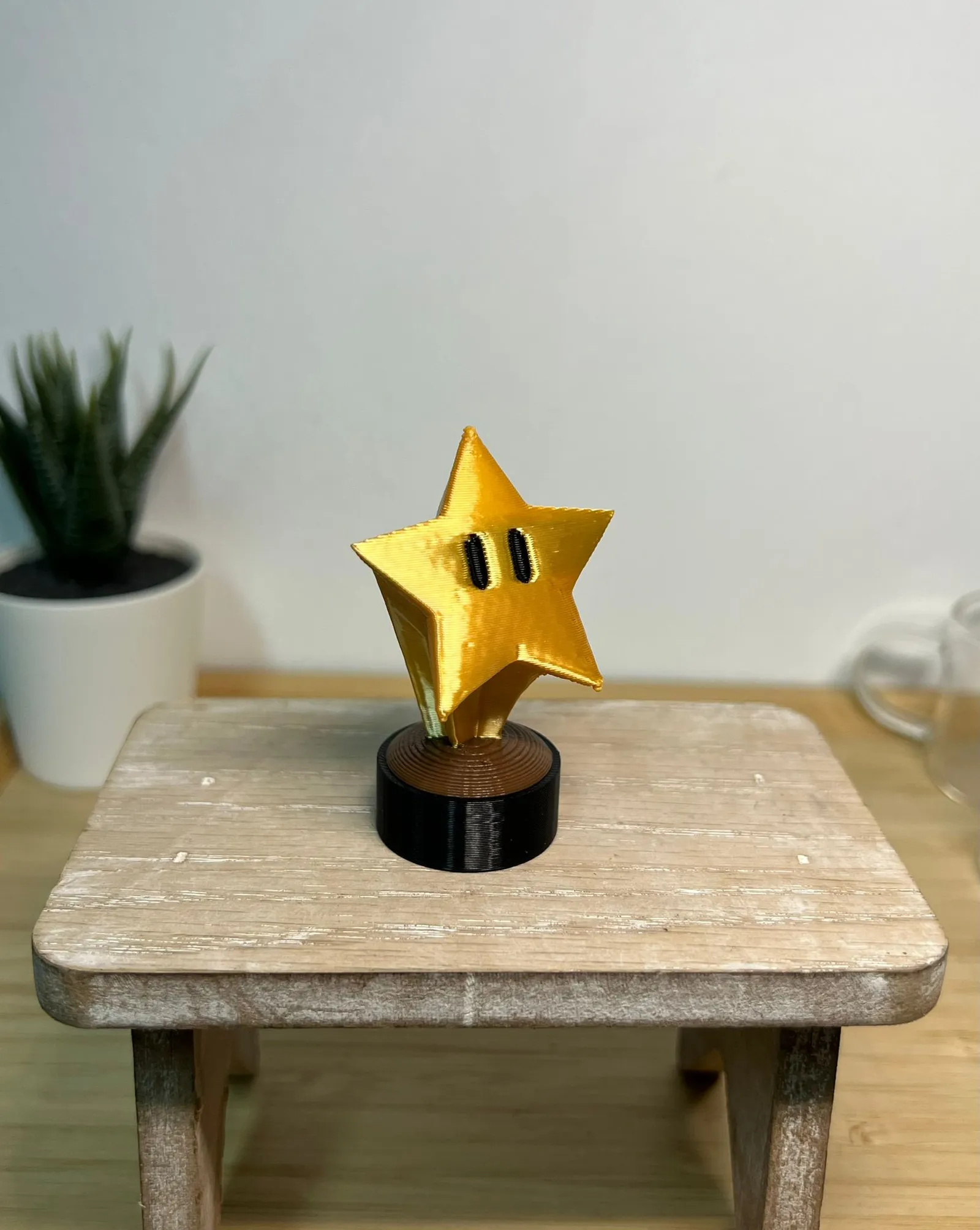 The finished gold star trophy, a cartoon star with two black eyes, on a round black and bronze base