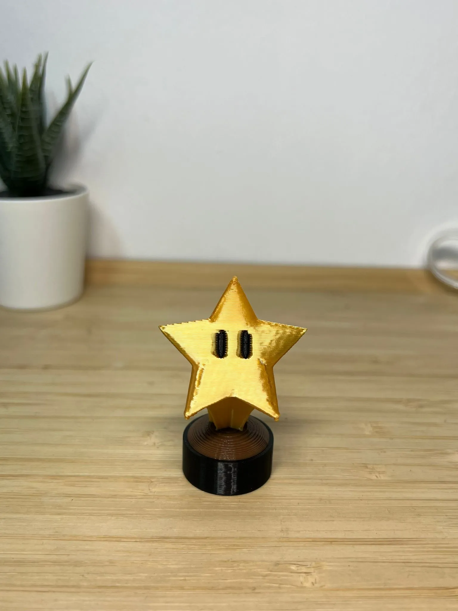 Front view of the gold star trophy on a wooden desk, the star's stem seated in the bronze top of its black base