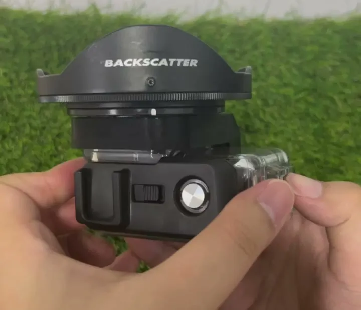 Side view of the wet lens on the black bracket above the dive housing, held in two hands