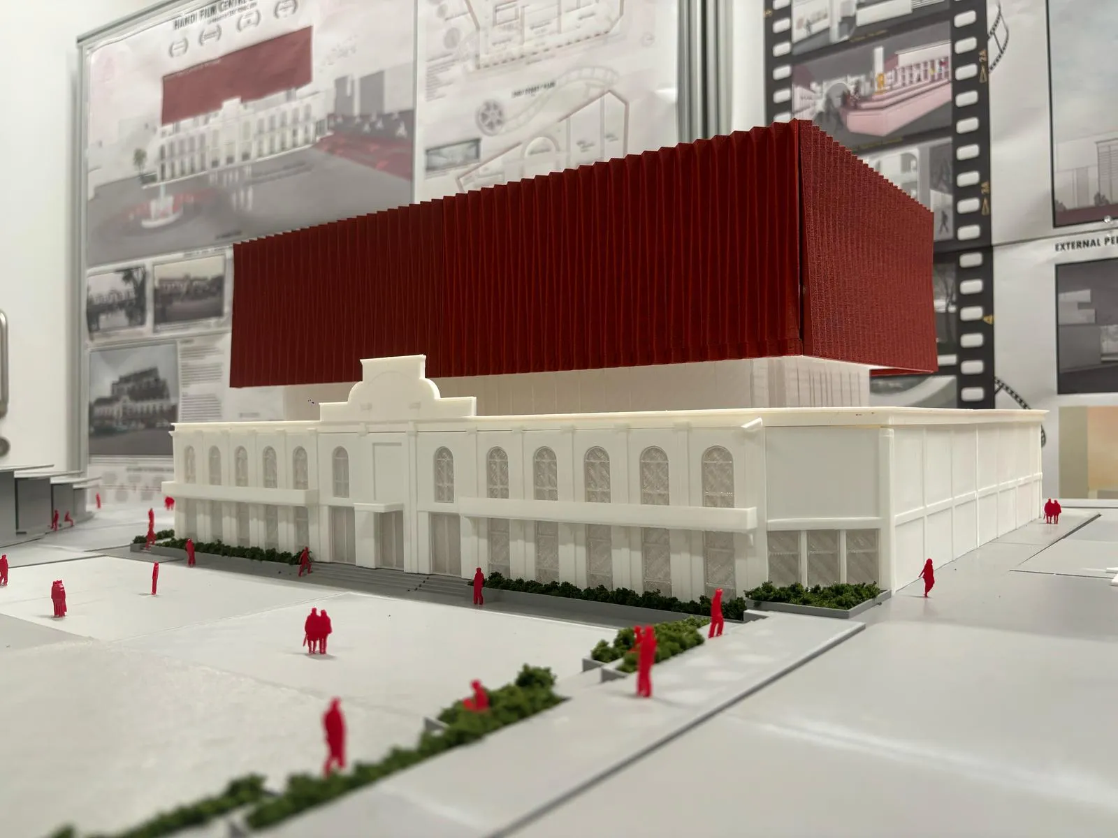 The model's front: a white building with arched windows and a central gable, a red fluted block above it, and red figures on the grey square