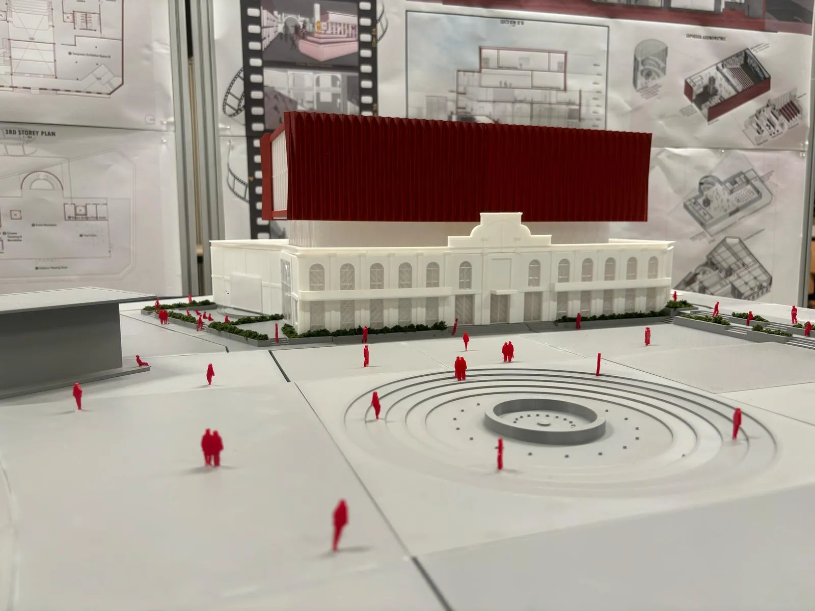 Low view across the round stepped plaza towards the white building and the red block, with figures on the square