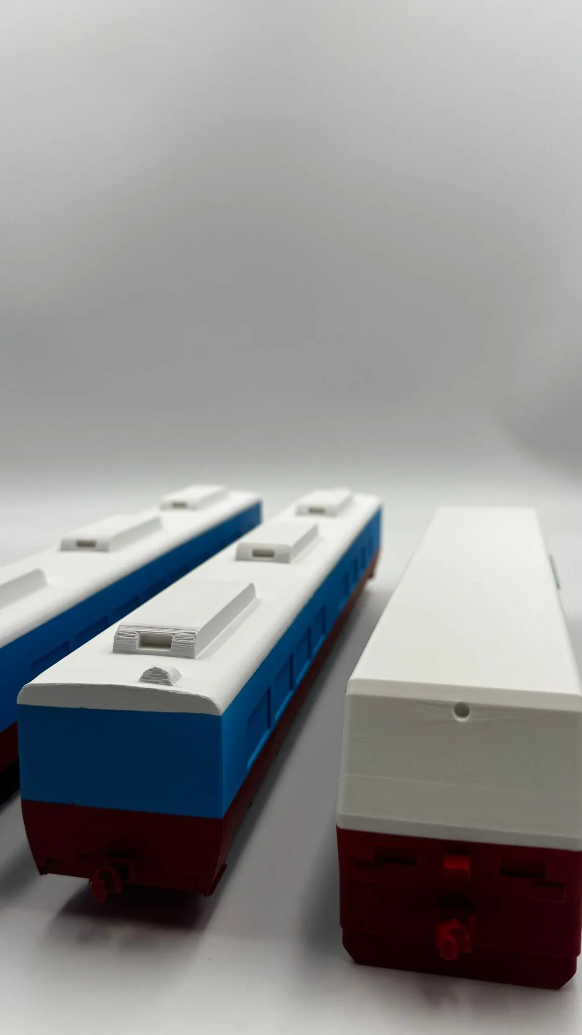 The end of the plain-roofed car close up, its white hood above a red front with a small coupler