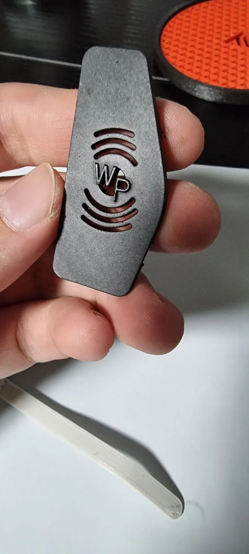 A hand holding a matt black vent cover cut with a sound-wave symbol around the initials WP