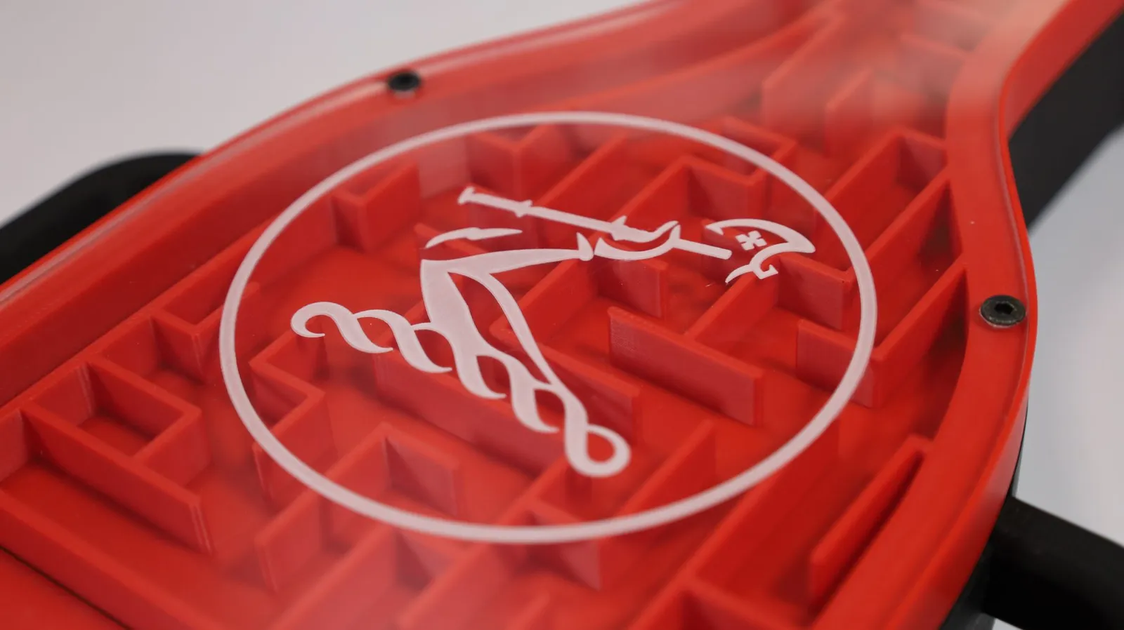 Close-up of the Hennessy rider emblem in white on the clear acrylic face, over the red printed maze walls