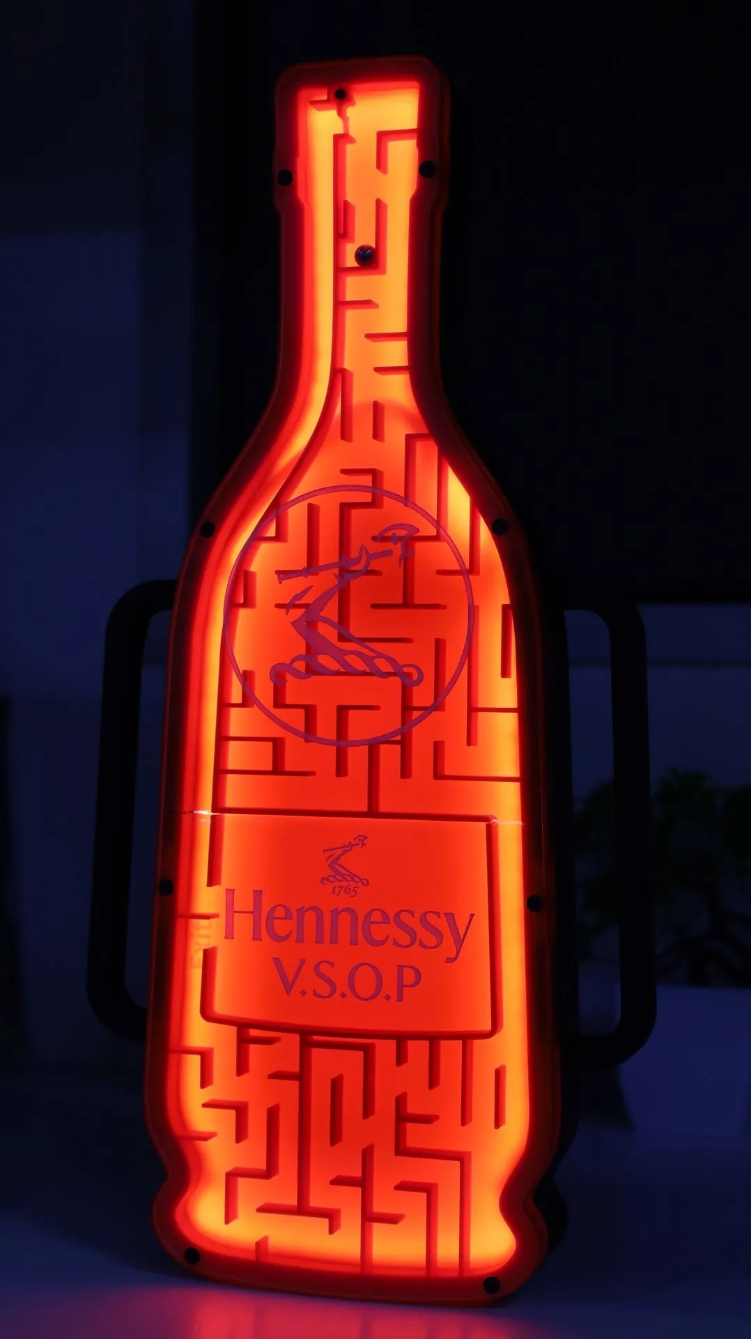 The finished maze standing upright in a dark room, glowing red from inside behind the Hennessy V.S.O.P logo and rider emblem