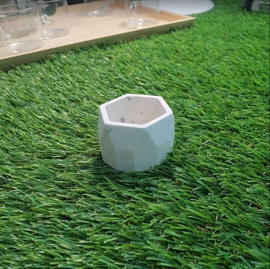 A plain white hexagonal Jesmonite planter with a few dark flecks, standing on artificial grass