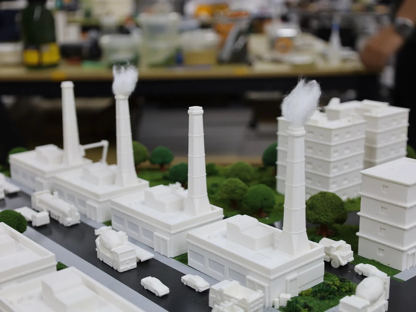 Factory chimneys with white smoke plumes rising above the sheds and trees of the industrial district