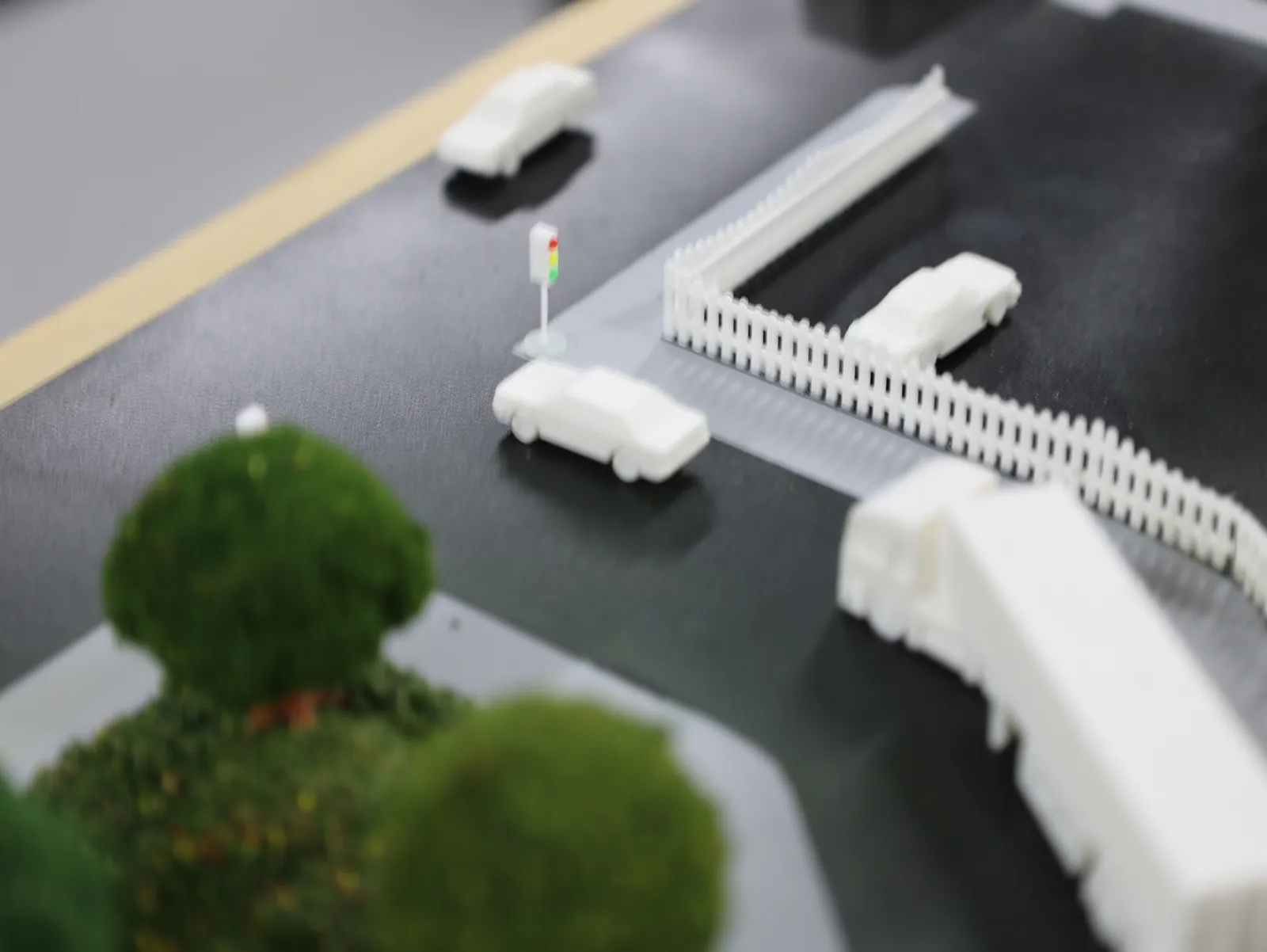 A street corner with a small traffic light, a white fence, parked cars and a truck beside a round tree