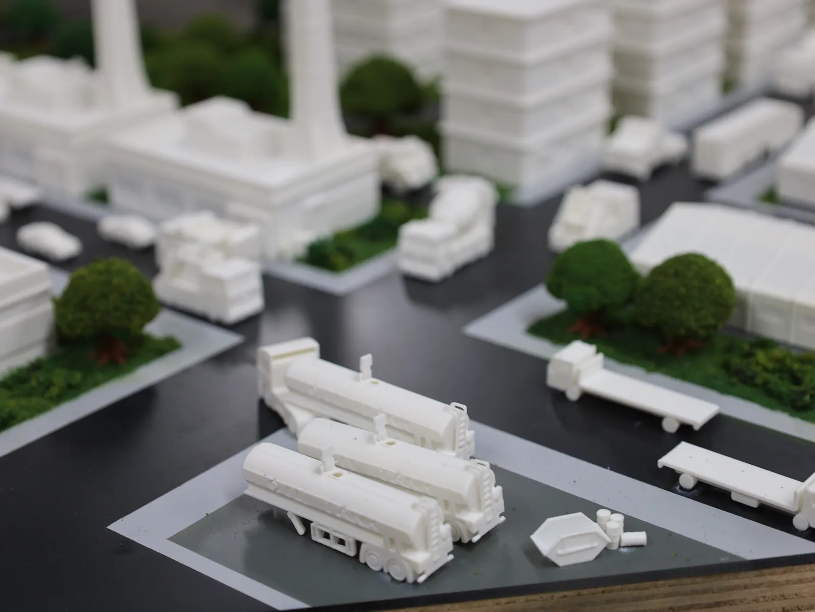 Printed tanker trucks, a flatbed trailer and a skip on a grey yard in the industrial district