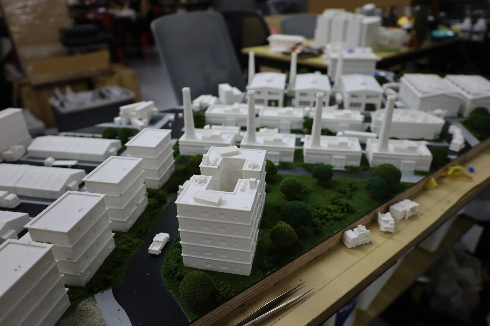 The industrial district mid-build: chimneys still without smoke, and loose printed vehicles waiting on the edge of the board beside tweezers