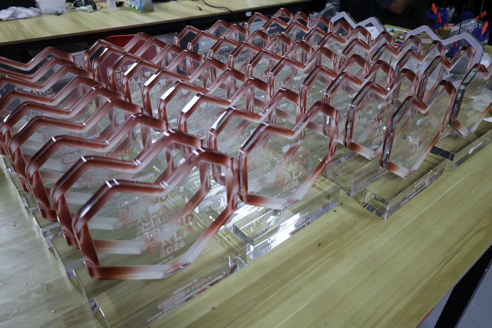 Rows of finished clear acrylic heart awards with rose-red edges, lined up on a workbench