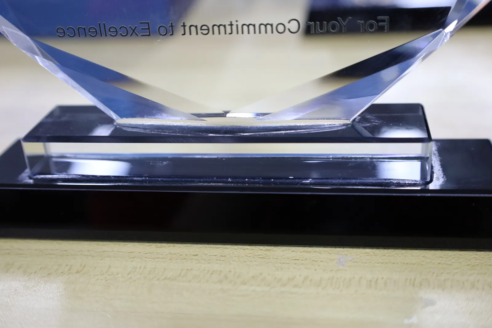 The foot of a faceted glass award standing in a clear block on a black base, with For Your Commitment to Excellence along the bottom of the disc