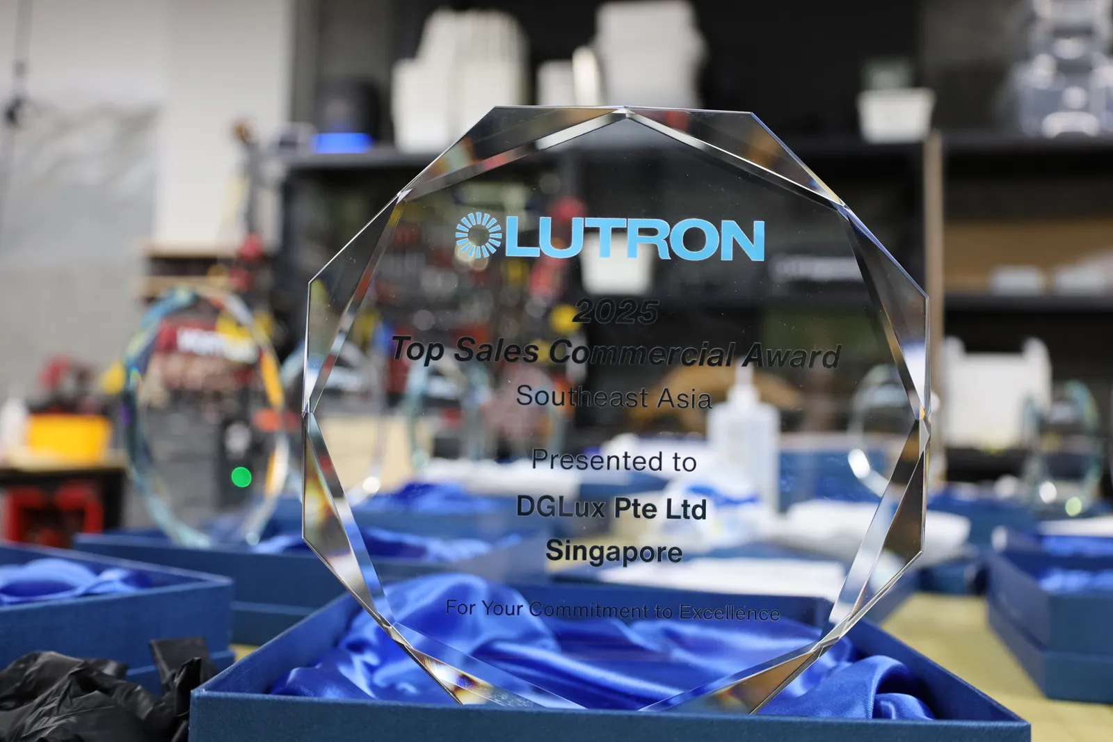 A Lutron 2025 Top Sales Commercial Award for DGLux Pte Ltd, Singapore, standing in an open blue box lined with blue satin