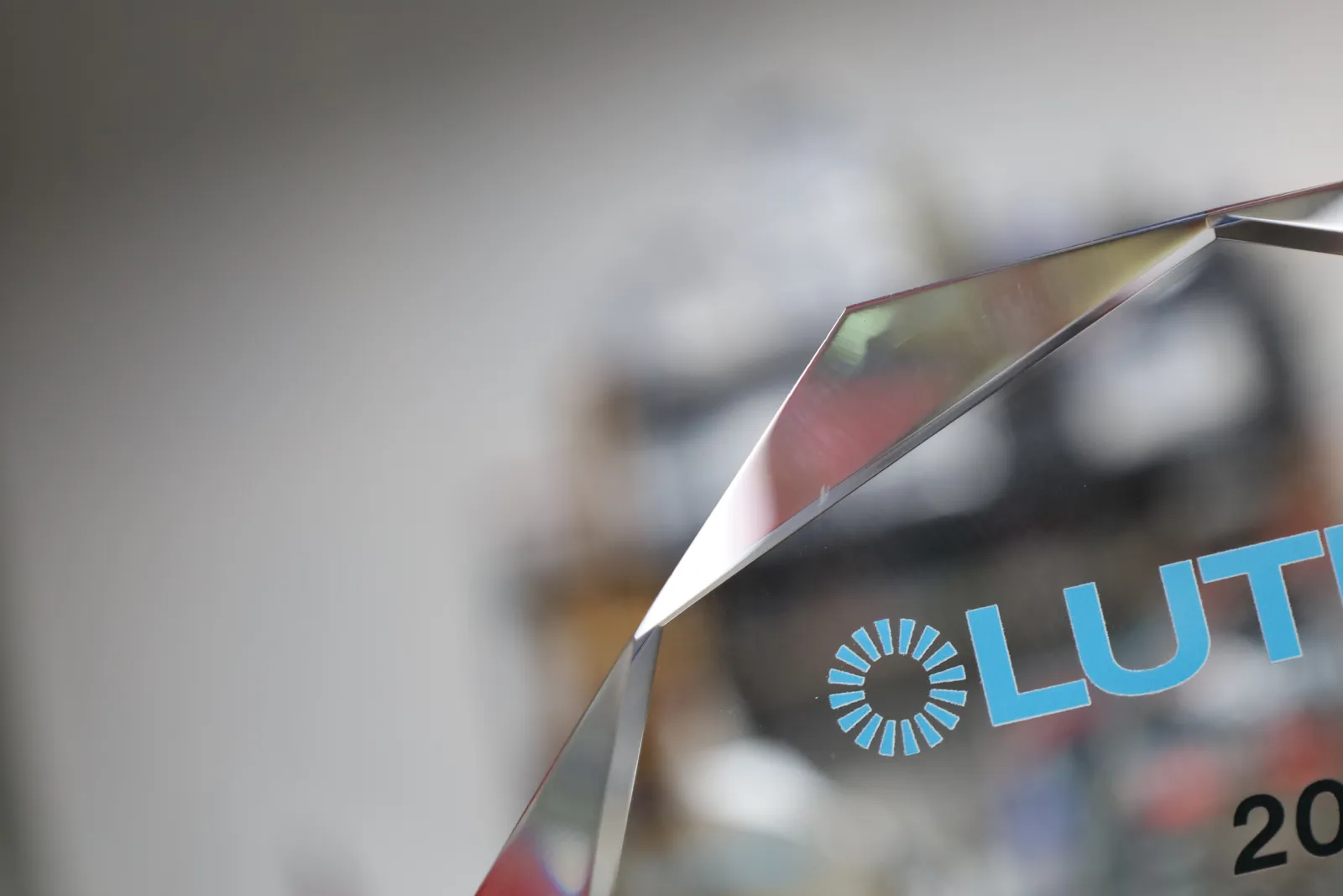 The blue Lutron logo on a clear glass award, beside one of its faceted edges