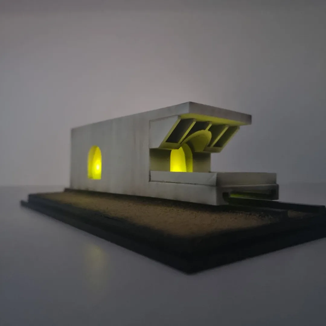 The model side on at eye level in a dim room, the arched window and the bay under the roof fins lit from inside, light showing under the carriage