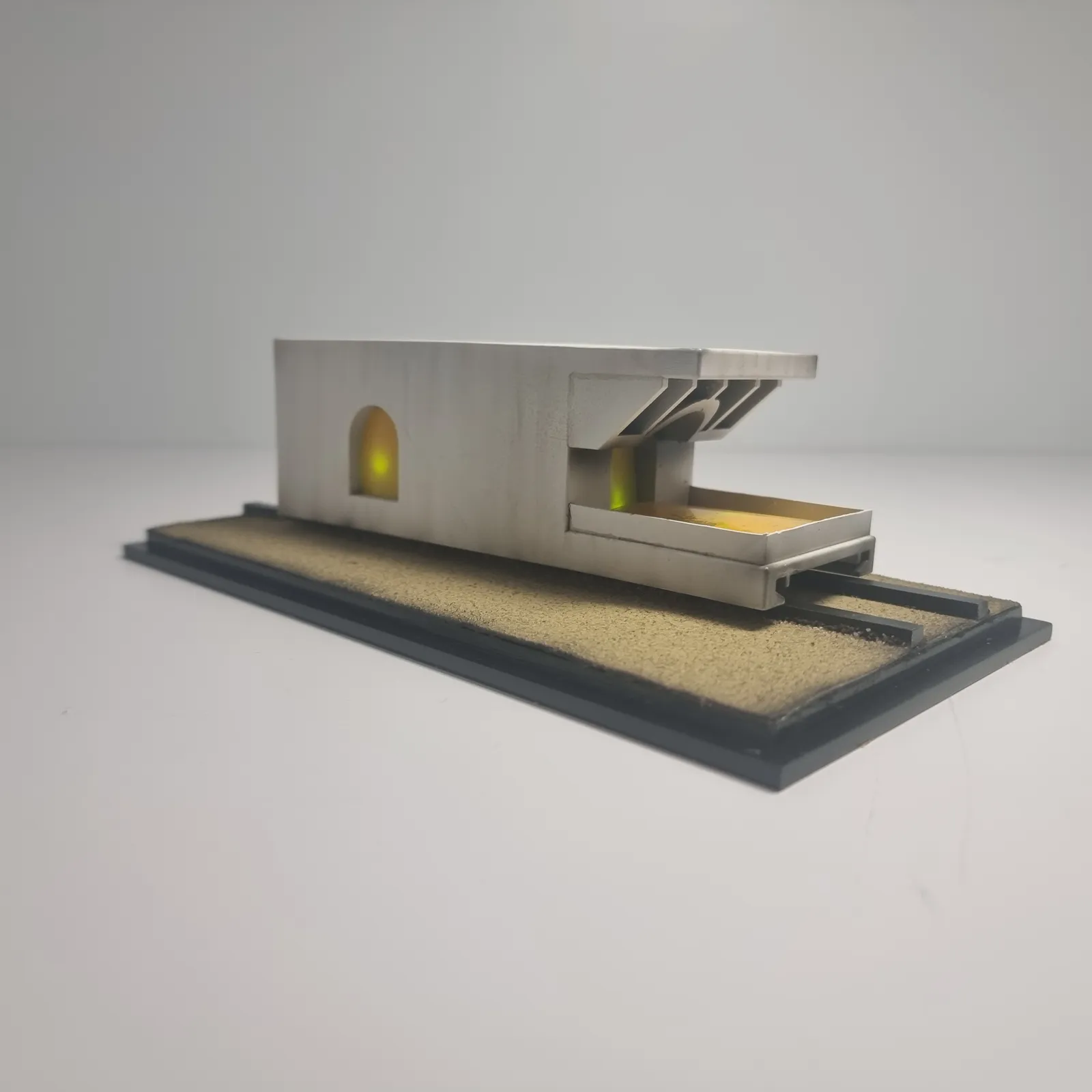 The model from the side at an angle: the long white carriage with its lit arched window, on a sand base with dark rails and a black edge