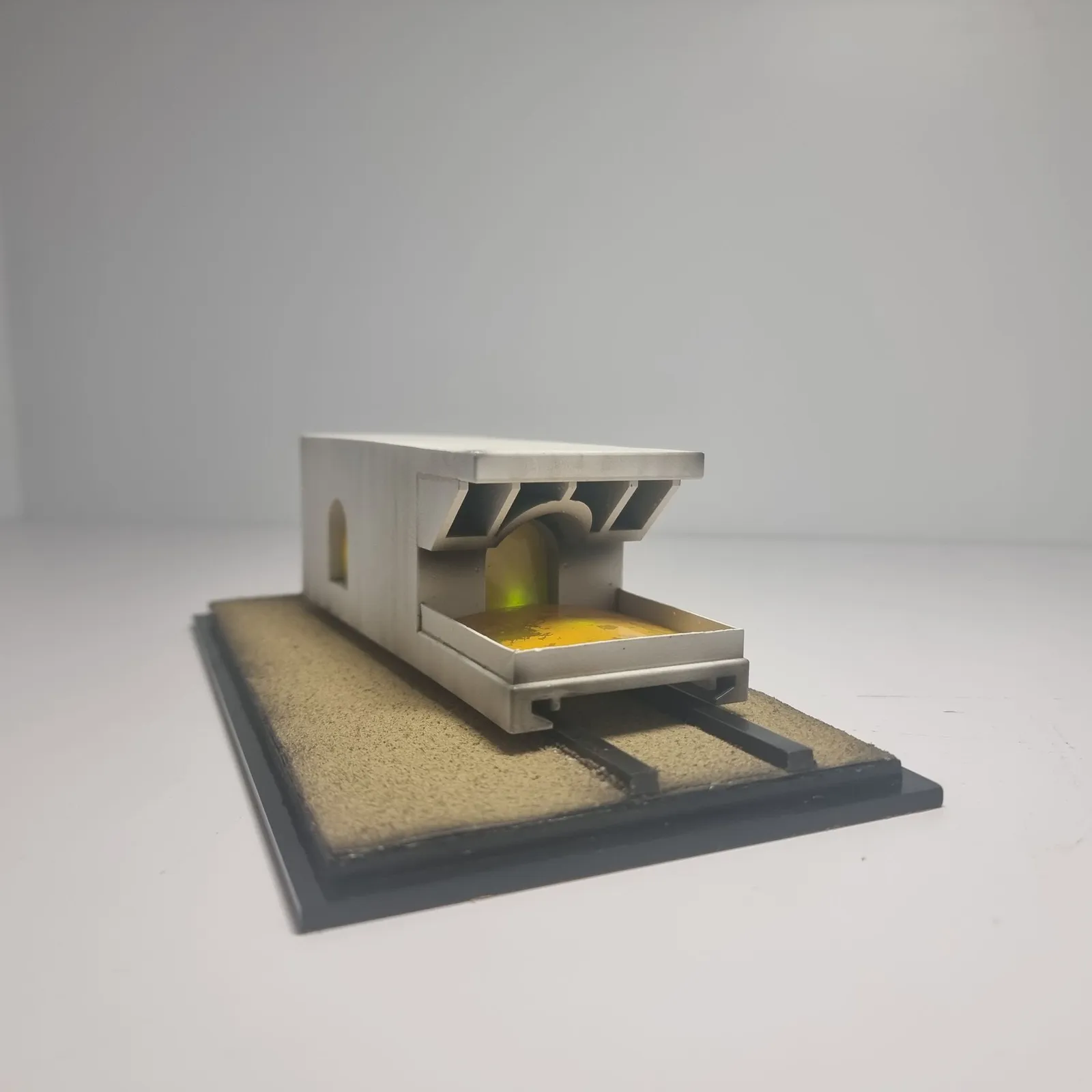 The finished model from the front at an angle: the white carriage with its open bay and angled roof fins, sitting over two dark rails on a sand base