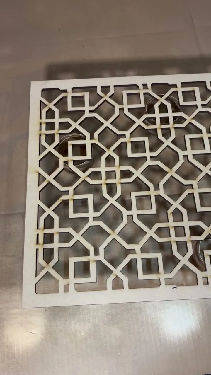 A bare wood panel cut in a lattice of interlocking squares, lying flat before spraying