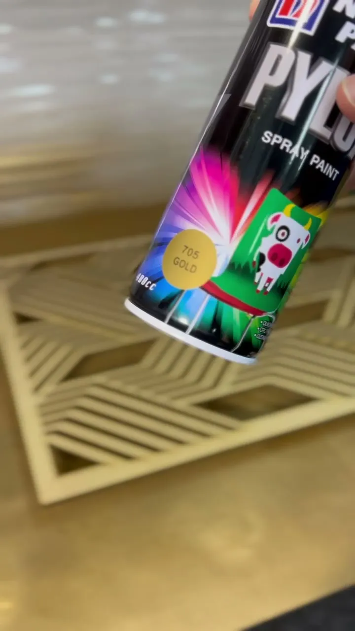 A can of gold spray held over the diagonal stripe panel in the booth