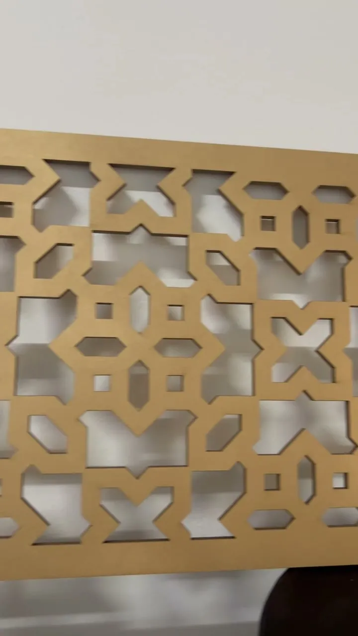 A gold panel cut in crosses and squares, held up against a white wall