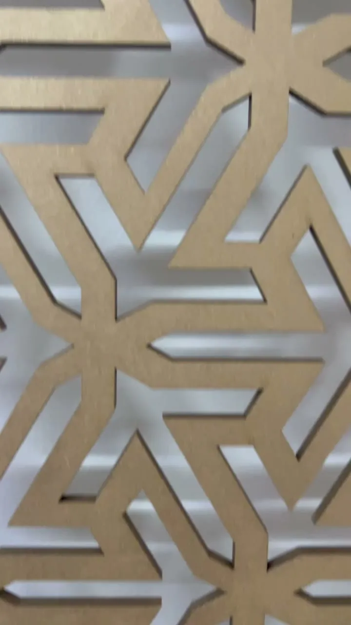 Close-up of a gold six-point star lattice, its shadow cast on the white wall behind