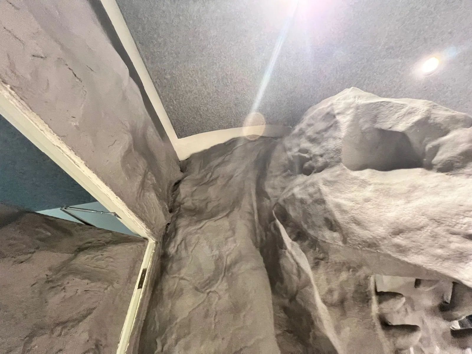 Close-up of the rock-textured wall meeting the pillar, the carved contours lit from the ceiling