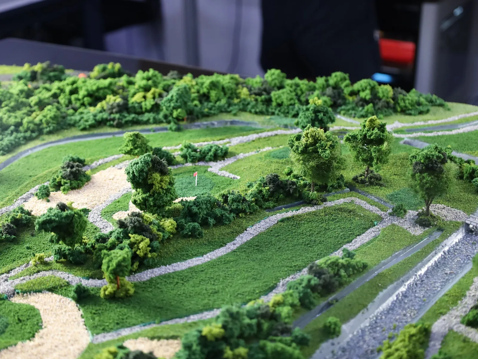 The finished diorama at a low angle across the fairways: gravel paths winding between greens and sand bunkers, trees, and a drain running down one side