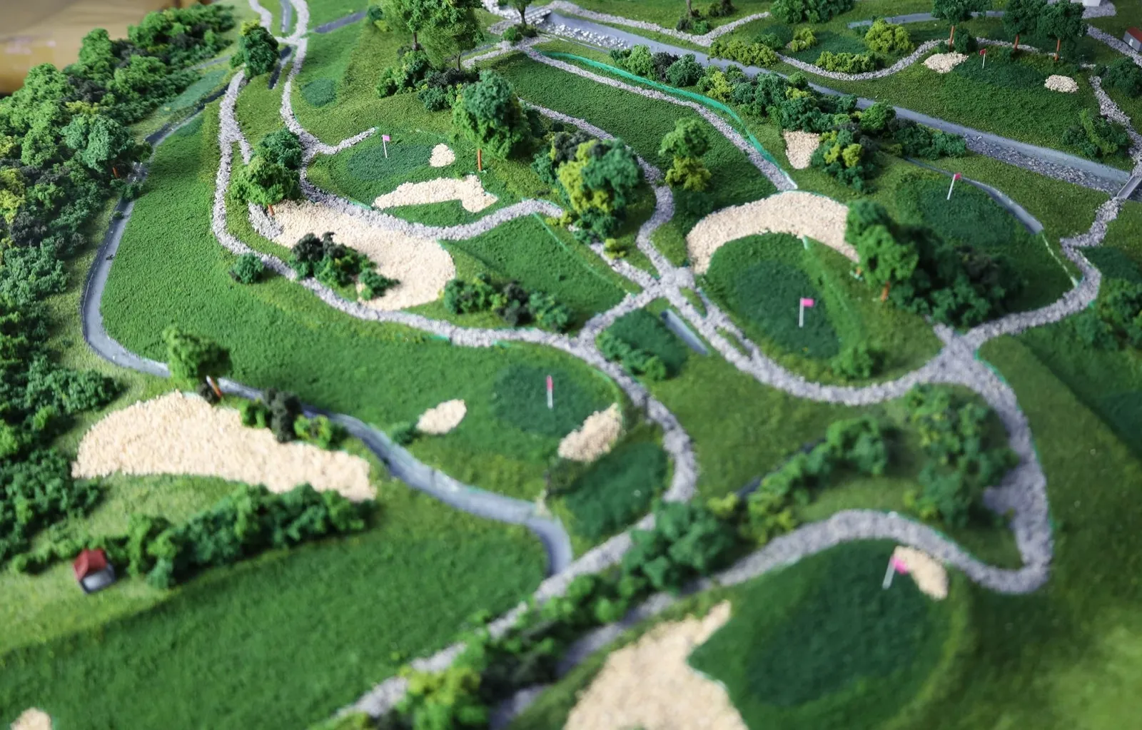 Close view across several holes: greens with pin flags, large sand bunkers and gravel paths winding between trees