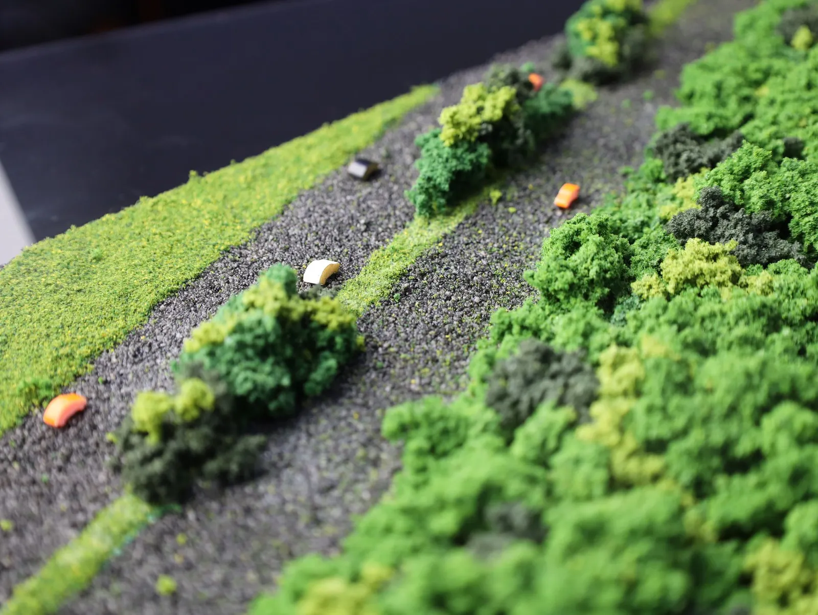 The road along the edge of the diorama, with tiny model cars on grey gravel between strips of trees