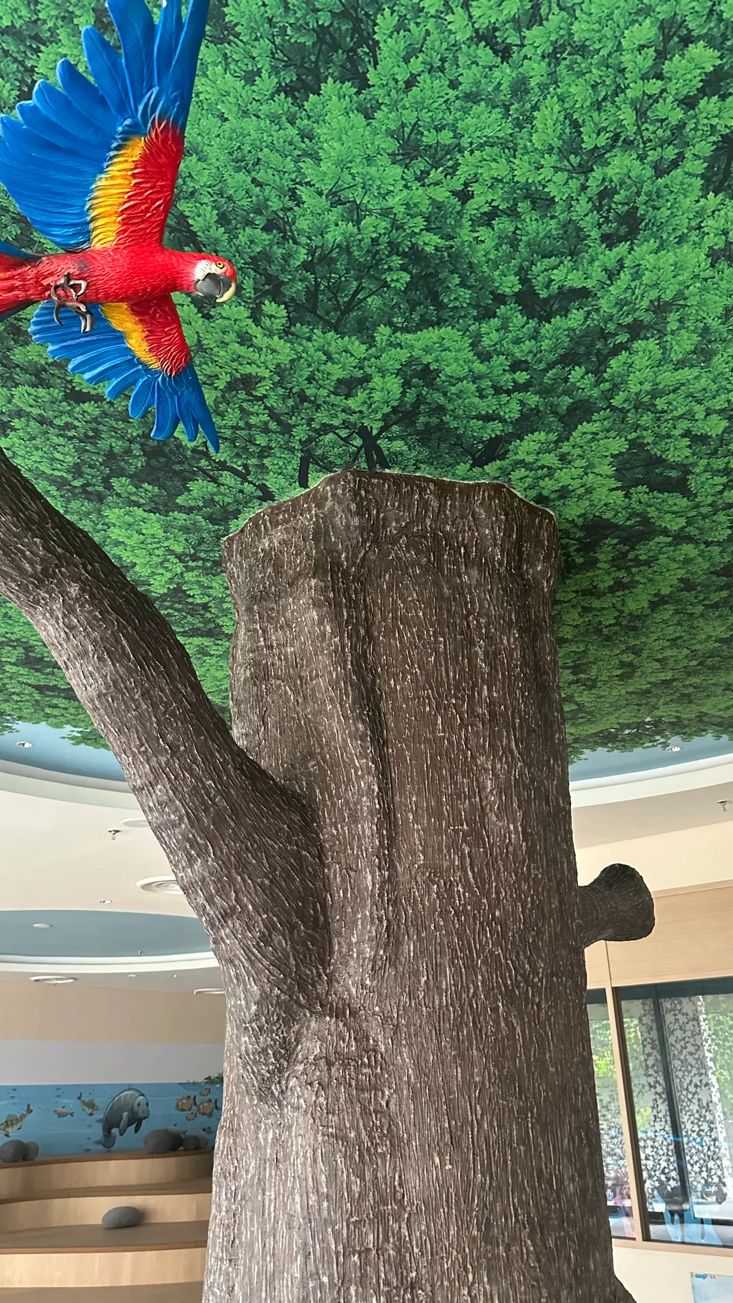 A red, yellow and blue macaw flying across the canopy mural above the painted trunk