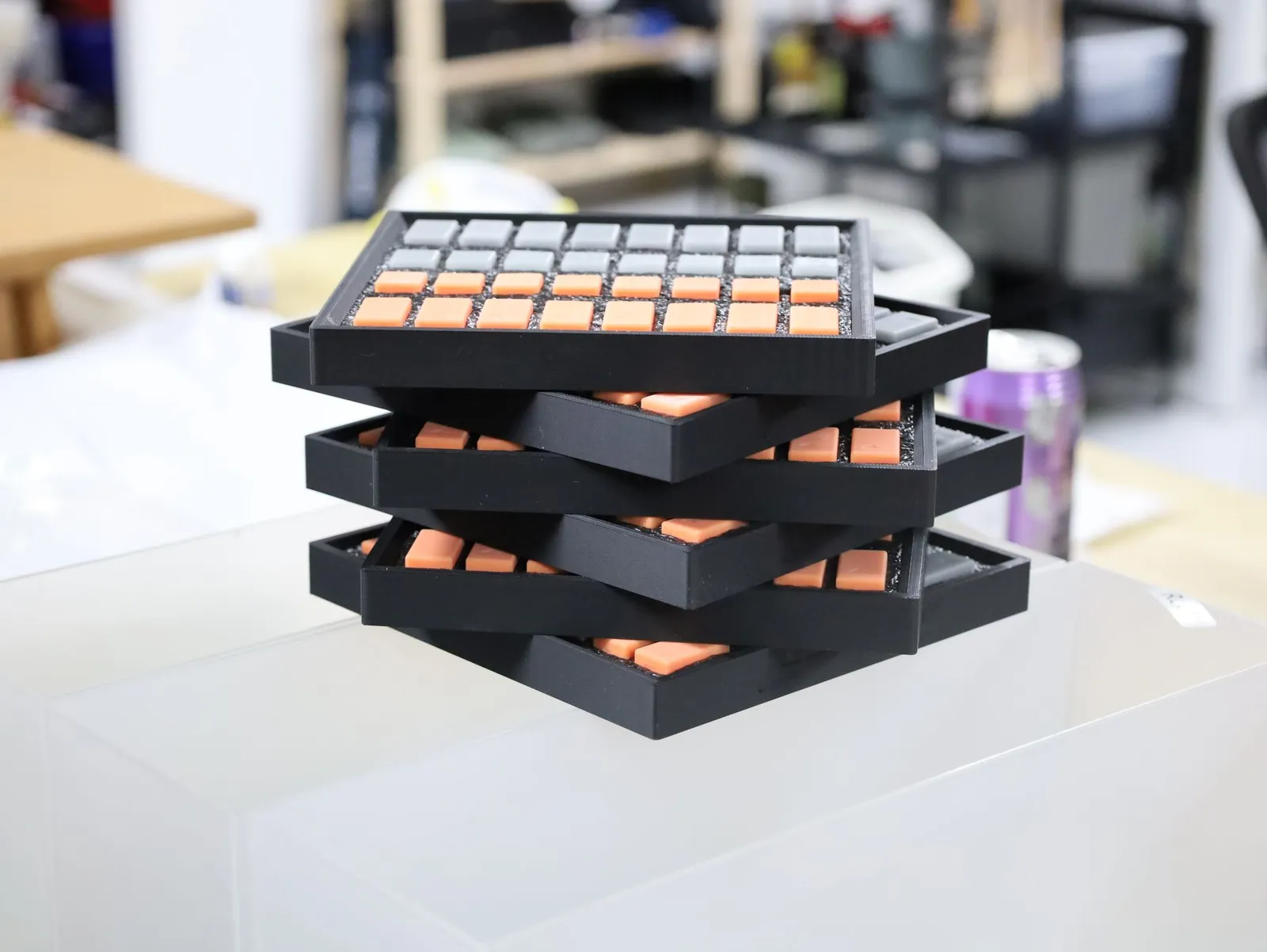 A stack of finished chess sets: black 3D printed trays, each filled with grey and orange pieces in black foam