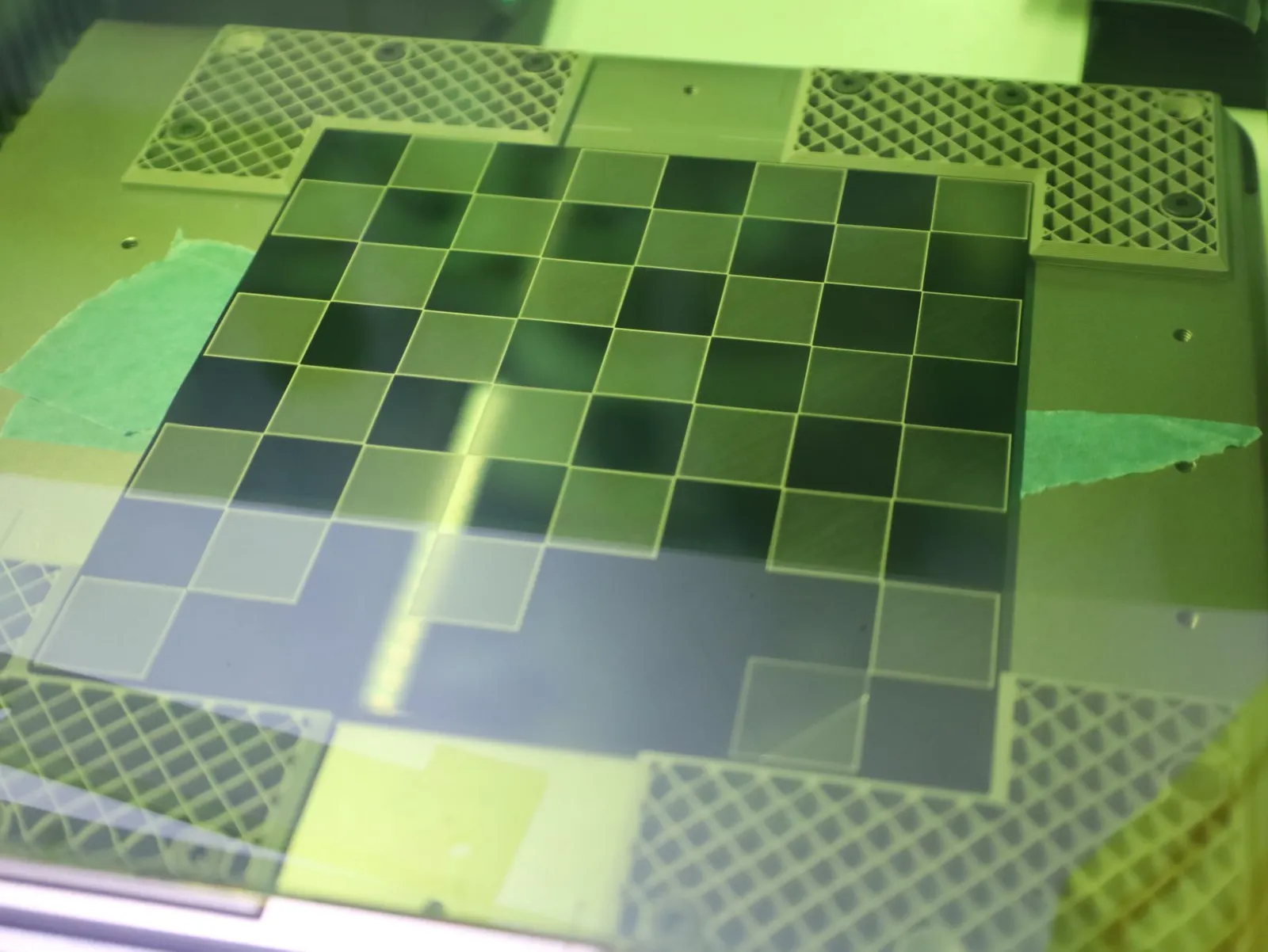 A chessboard of light and dark squares being 3D printed on the build plate, seen through the printer window