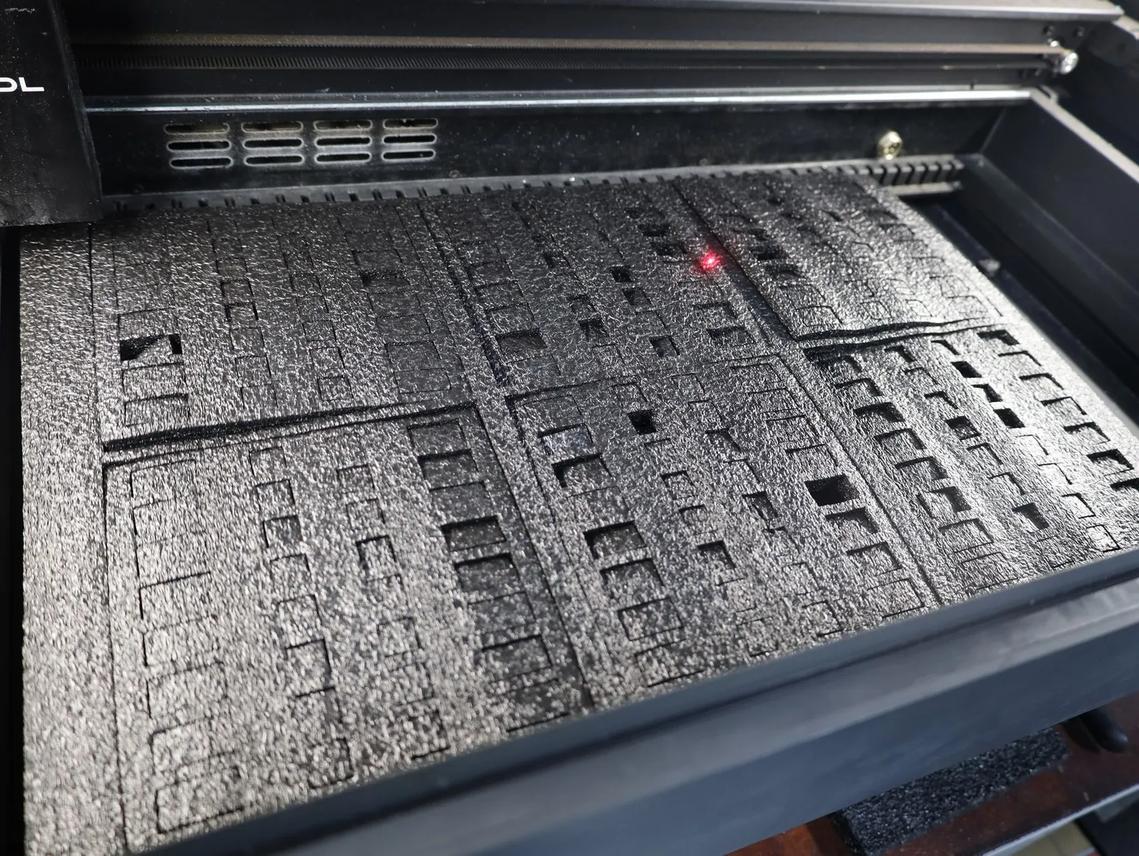 A sheet of black foam on the laser cutter bed, cut into tray inserts with rows of rectangular pockets