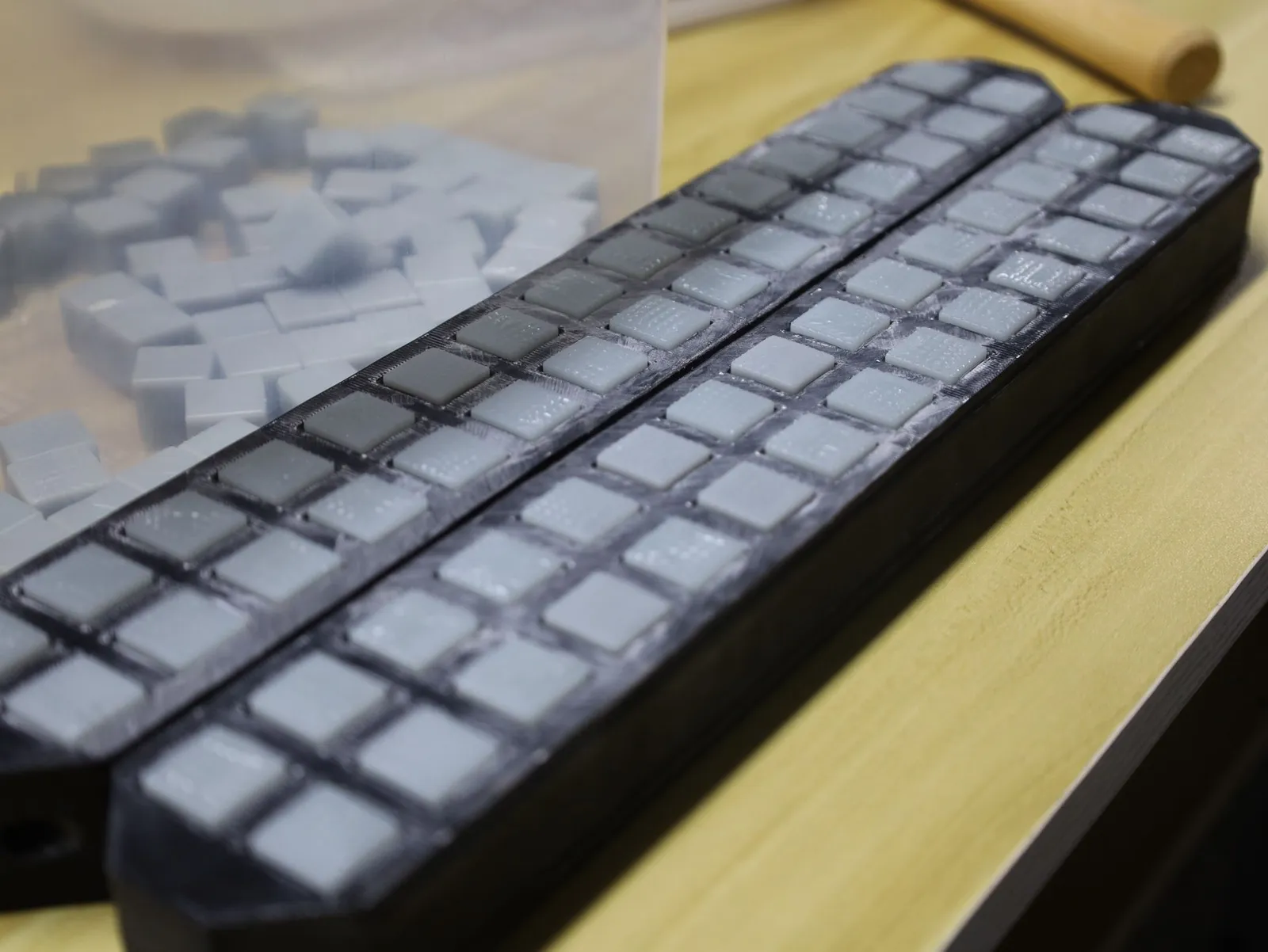 Grey chess pieces sitting in rows in two black 3D printed jigs on a workbench