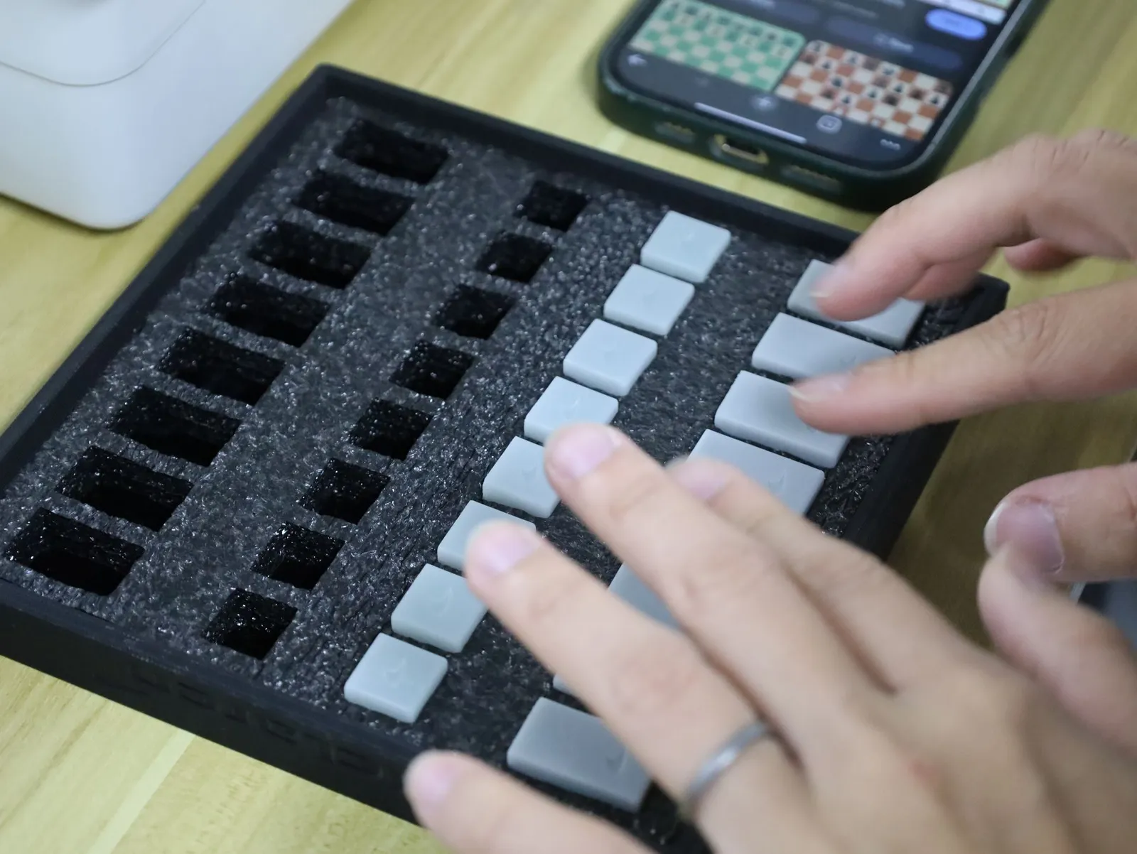 Hands pressing grey pieces into the foam pockets of a black tray