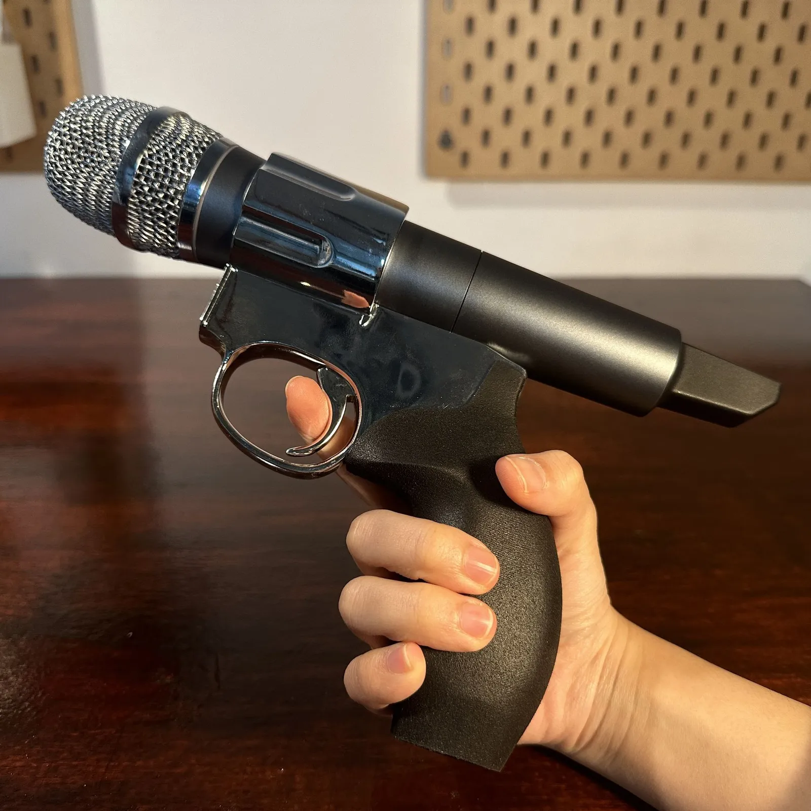 The finished prop held side on, a finger in the chrome trigger guard and the microphone lying along the top